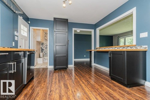Kitchen featuring wood-finish flooring, dark cabinetry with bar pulls, butcher block countertops, and a mosaic tile backsplash - 13411 140 Street, Edmonton, AB 