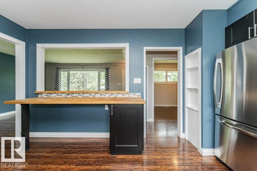 Kitchen area featuring wood-finish flooring, a stainless steel refrigerator, and a breakfast bar with a butcher block countertop and black cabinetry - 13411 140 Street, Edmonton, AB 