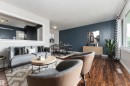 Open-concept living area featuring rich wood-finish flooring, a prominent accent wall, and a large window providing natural light - 13411 140 Street, Edmonton, AB 