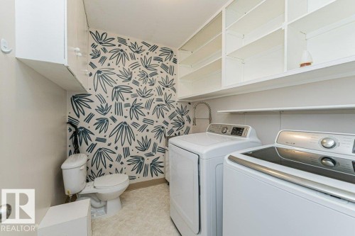 Laundry room featuring patterned wall covering, built-in shelving, white cabinetry, and a utility sink - 13411 140 Street, Edmonton, AB 