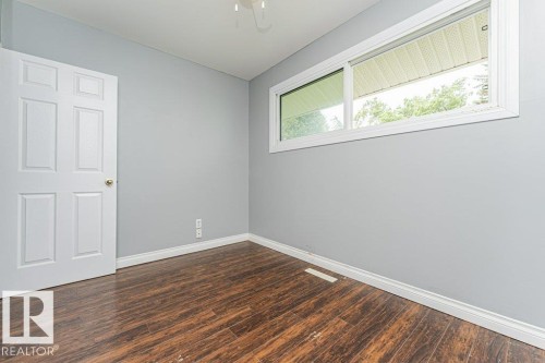 Spacious room featuring wood-finish flooring, light gray walls, white trim, and a white six-panel door with a brass knob - 13411 140 Street, Edmonton, AB 