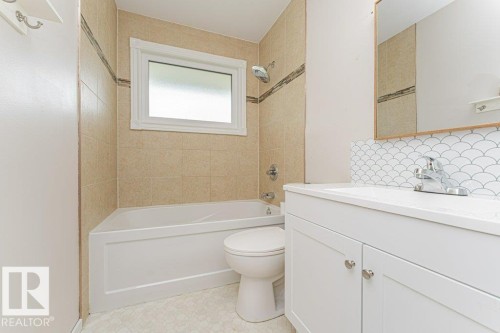 Bathroom featuring a white vanity with a single basin sink, contemporary chrome faucet, and a decorative scallop tile backsplash - 13411 140 Street, Edmonton, AB 