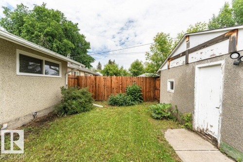 Expansive grassy area featuring a wood privacy fence, established perimeter shrubs, and concrete walkway - 13411 140 Street, Edmonton, AB 