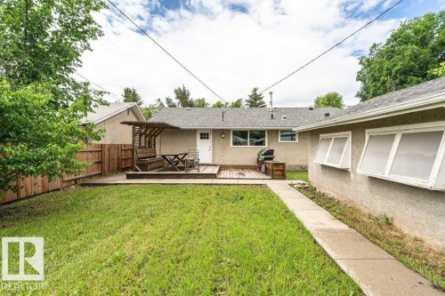 Spacious backyard with a wooden fence, concrete pathway, and a deck featuring a pergola - 13411 140 Street, Edmonton, AB 