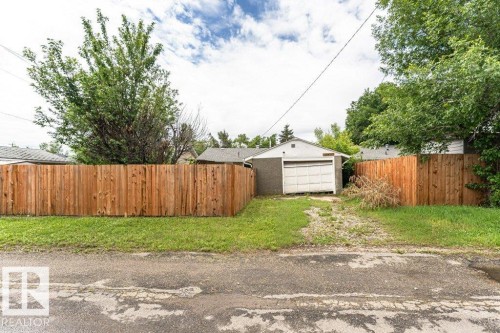 Detached garage with a paneled door, surrounded by a wood privacy fence and mature trees - 13411 140 Street, Edmonton, AB 