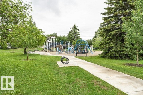 Expansive green space featuring a concrete pathway, mature trees, a multi-structure playground, and swing sets - 13411 140 Street, Edmonton, AB 