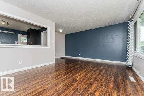 Spacious room featuring rich wood-finish flooring, a prominent accent wall, and a large window offering ample natural light - 13411 140 Street, Edmonton, AB 