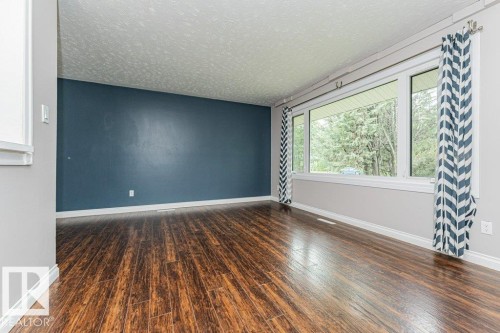 Expansive room featuring wood-finish flooring, a full-wall window, and a dark accent wall - 13411 140 Street, Edmonton, AB 