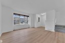Bright living space featuring expansive windows, wood-finish flooring, a white paneled entry door with decorative glass, and a carpeted staircase - 2143 32 Street, Edmonton, AB 