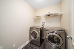Dedicated laundry area featuring dark tiled flooring, light wall paint, white baseboards, and a wire shelving unit - 