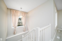 Stairway landing with a window featuring a built-in bench, a suspended ceiling light fixture, and white painted railings - 