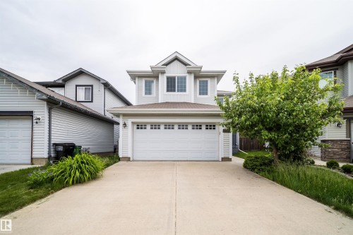 Two-story residence featuring light-colored siding, a prominent front-facing gable, and an attached two-car garage with divided light windows - 11312 13 Ave Sw, Edmonton, AB 