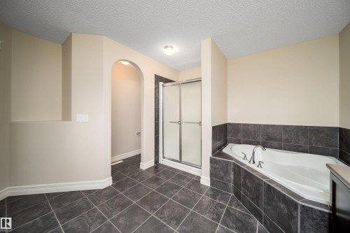 Bathroom featuring dark grey tile flooring, a built-in soaking tub with dark grey tile surround, a glass-enclosed shower, and an arched alcove - 11312 13 Ave Sw, Edmonton, AB 