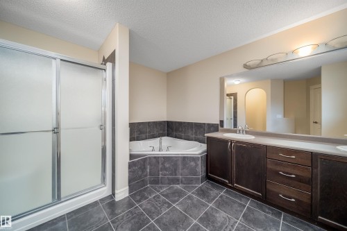 Bathroom featuring a corner soaking tub, a dark wood-finish vanity with dual sinks, a large wall-mounted mirror, and a stand-up shower with frosted glass doors - 11312 13 Ave Sw, Edmonton, AB 