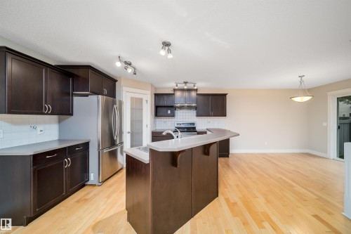 Modern kitchen featuring dark wood cabinetry, stainless steel appliances, light countertops, and a central island with an integrated breakfast bar - 11312 13 Ave Sw, Edmonton, AB 