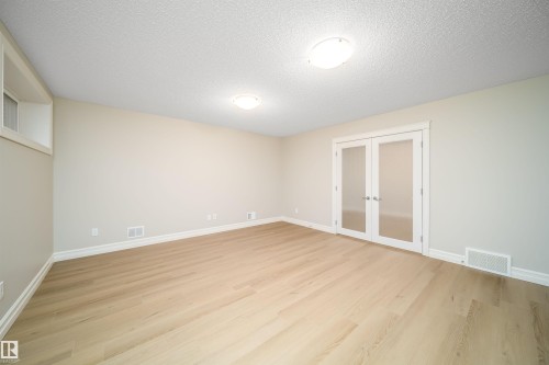 Spacious room featuring light wood-finish flooring, neutral wall tones, and white baseboards - 11312 13 Ave Sw, Edmonton, AB 
