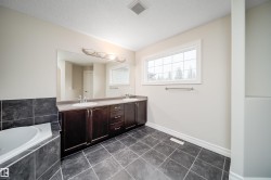 Full-size bathroom featuring a double vanity with ample storage, a large soaking tub with dark tile surround, a spacious window, and dark tiled flooring - 
