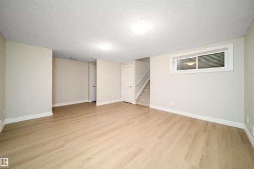 Spacious room featuring wood-finish flooring, neutral-toned walls, and white baseboards - 11312 13 Ave Sw, Edmonton, AB 
