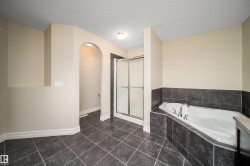 Bathroom featuring dark grey tile flooring, a built-in soaking tub with dark grey tile surround, a glass-enclosed shower, and an arched alcove - 