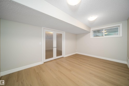 Well-lit room featuring wood-finish flooring, white baseboards, and a neutral wall color - 11312 13 Ave Sw, Edmonton, AB 