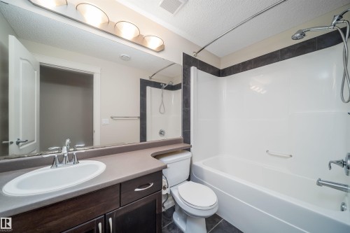 Full bathroom featuring a dark wood-finish vanity with an integrated sink, polished chrome faucet, and a large wall-mounted mirror - 11312 13 Ave Sw, Edmonton, AB 
