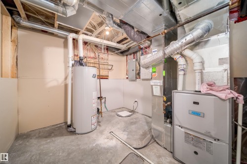 Utility room featuring a water heater, furnace system, exposed ductwork, and unfinished concrete flooring - 11312 13 Ave Sw, Edmonton, AB 