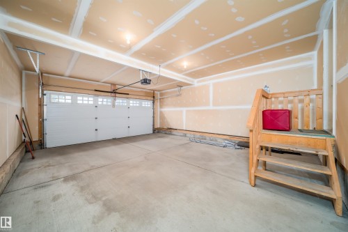 Spacious garage featuring a concrete floor, an overhead garage door with window inserts, and exposed ceiling joists - 11312 13 Ave Sw, Edmonton, AB 