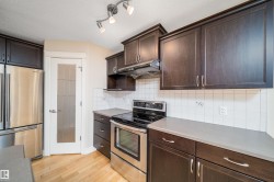 Full kitchen featuring dark wood cabinetry, stainless steel appliances, light countertops, white tile backsplash, and wood-finish flooring - 
