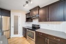 Full kitchen featuring dark wood cabinetry, stainless steel appliances, light countertops, white tile backsplash, and wood-finish flooring - 11312 13 Ave Sw, Edmonton, AB 
