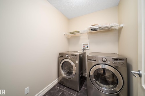 Dedicated laundry area featuring dark tiled flooring, light wall paint, white baseboards, and a wire shelving unit - 11312 13 Ave Sw, Edmonton, AB 