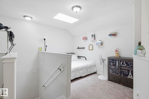 Carpeted loft area featuring a skylight, two flush-mount ceiling lights, a white baluster and newel post, and a partial wall with handrail - 426 3425 19 Street, Edmonton, AB 