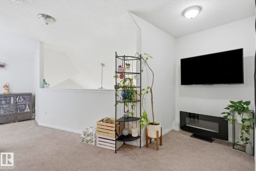 Carpeted interior with light-colored walls, featuring a low wall partition and a built-in electric fireplace - 426 3425 19 Street, Edmonton, AB 
