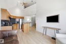 Open-concept living area featuring vaulted ceilings, light wood-finish flooring, a kitchen with wood cabinetry and dark countertops, and a mezzanine balcony overhead - 426 3425 19 Street, Edmonton, AB 