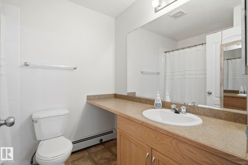 Bathroom featuring a wood-finish vanity with an integrated sink, a full-width mirror, and a white toilet - 426 3425 19 Street, Edmonton, AB 