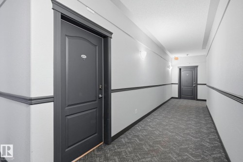 Hallway with textured gray carpeting, white walls, and dark gray wainscoting - 426 3425 19 Street, Edmonton, AB 