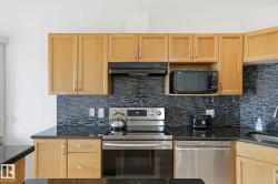 Kitchen featuring light wood cabinetry, dark countertops, a mosaic tile backsplash, and stainless steel appliances including a range and dishwasher - 
