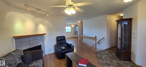 Living area featuring a tiled fireplace with wood mantel, track lighting, and a ceiling fan with integrated lighting - 4519 59 Ave, Vegreville, AB 