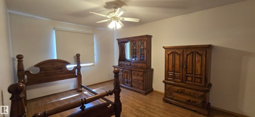 Room featuring wood-finish flooring, a ceiling fan with integrated lighting, and a window with a roller shade - 4519 59 Ave, Vegreville, AB 