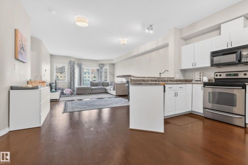 Open-concept living area featuring a kitchen with white cabinetry, stainless steel appliances, and stone-finish countertops - 226 4304 139 Avenue, Edmonton, AB 