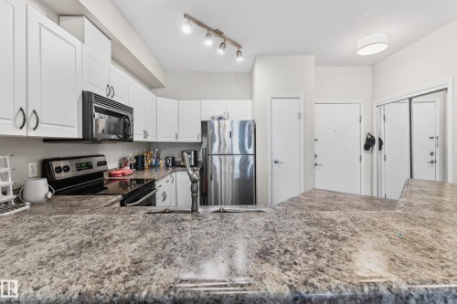 Kitchen featuring extensive countertop space, white cabinetry, stainless steel refrigerator, black range, and built-in microwave - 226 4304 139 Avenue, Edmonton, AB 