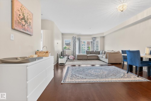 Expansive open-concept living area featuring rich wood-finish flooring, a contemporary chandelier, and large windows with decorative drapery - 226 4304 139 Avenue, Edmonton, AB 