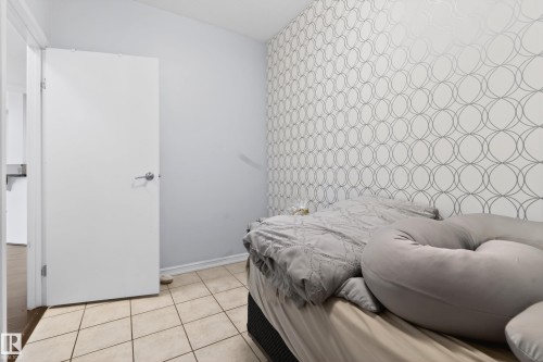 Room featuring a decorative accent wall with a geometric circular pattern, light-toned tile flooring, and a white interior door with a chrome handle - 226 4304 139 Avenue, Edmonton, AB 