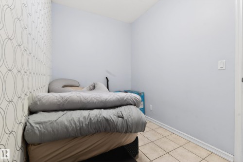 Room featuring a decorative accent wall with a geometric pattern, painted light blue walls, and light-toned square floor tiles - 226 4304 139 Avenue, Edmonton, AB 