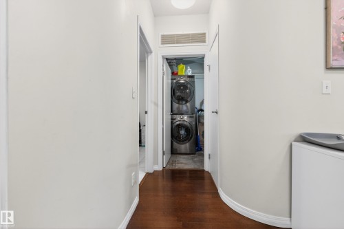 Dedicated laundry area featuring a stacked washer and dryer, wood-finish flooring, and white baseboards - 226 4304 139 Avenue, Edmonton, AB 