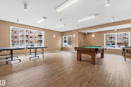 Spacious recreation room featuring wood-finish flooring, ample natural light from multiple large windows, and a combination of recessed and flush-mounted ceiling lighting - 226 4304 139 Avenue, Edmonton, AB 