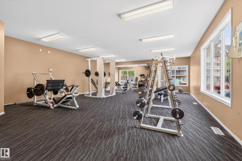 Fitness center featuring multiple weight machines, a free weight rack, patterned carpet flooring, and large windows - 226 4304 139 Avenue, Edmonton, AB 