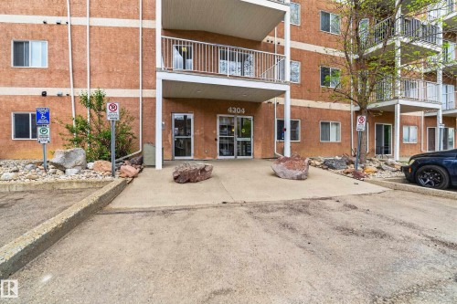 Building exterior with textured brown stucco, multiple white balconies with metal railings, and a main entrance featuring double glass doors - 226 4304 139 Avenue, Edmonton, AB 