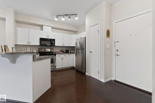 Kitchen featuring white cabinetry, stainless steel appliances, dark wood-finish flooring, and a stone-finish countertop - 226 4304 139 Avenue, Edmonton, AB 