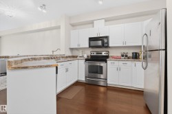 Kitchen featuring white cabinetry, light granite-finish countertops, stainless steel appliances, a corner sink with a high-arch faucet, and wood-finish flooring - 
