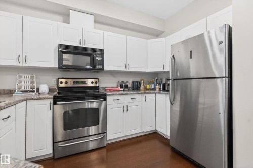 Kitchen featuring white cabinetry, wood-finish flooring, stainless steel appliances, and light-colored countertops - 226 4304 139 Avenue, Edmonton, AB 